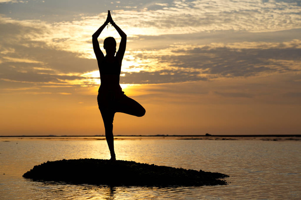 Силует молода жінка практикує йогу на пляжі на сході сонця
. - Фото, зображення