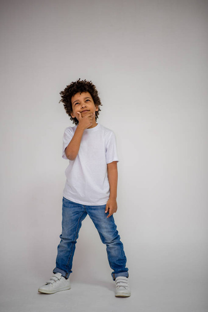 dark-skinned boy in blue jeans and in a white sweater in different poses shows different emotions on different backgrounds - Фото, изображение