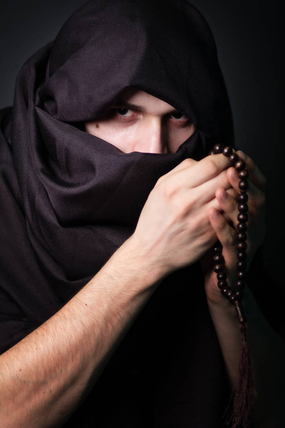 Arab człowiek z surowym spojrzeniem. Facet z zamkniętych twarz. Czarne ubrania. Mężczyzna w czarnym hidżab. Portret z muzułmaninem. - Zdjęcie, obraz