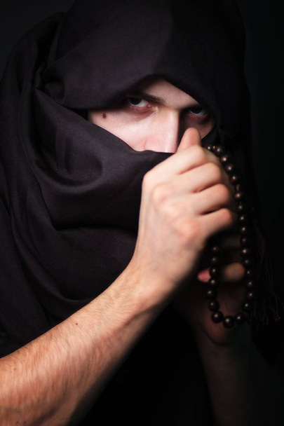 Hombre árabe con una mirada severa. El tipo con la cara cerrada. Ropa negra. El hombre del hiyab negro. Retrato de estudio de un musulmán
. - Foto, imagen