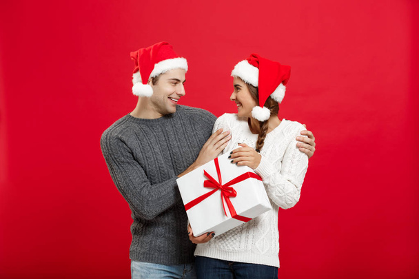Christmas Concept - Young woman covering mans eyes with hand and giving surprise big gift. Isolated on Red background - Foto, Imagem