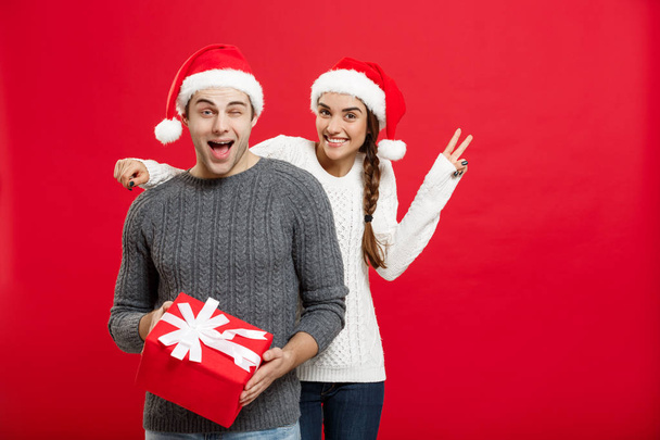 Christmas Concept - Young woman covering mans eyes with hand and giving surprise big gift. Isolated on Red background - Foto, immagini