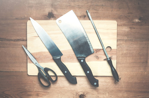 Kitchen knifes with sharpener and scissor on a wood background. - Photo, image
