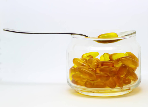 Aceite de hígado de bacalao omega 3 cápsulas de gel de vitamina e aisladas sobre fondo blanco en una botella de vidrio transparente con una cuchara de acero
 - Foto, imagen