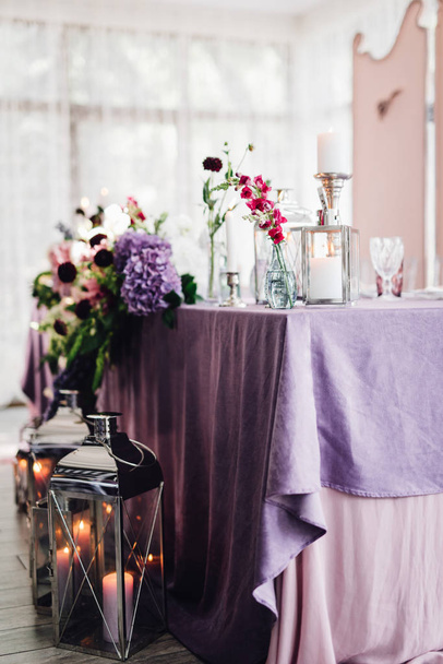 Primer plano de la mesa festiva cubierta con tela violeta y flores decoradas con velas
 - Foto, imagen