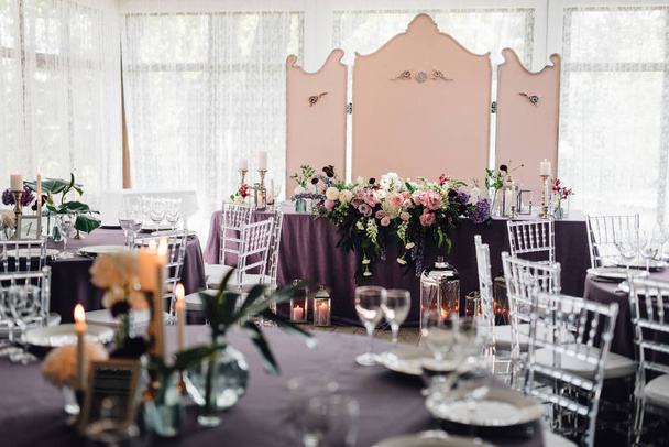 Valoisa ravintola pöydät peitetty violetti kangas ja kukkia koristeltu kynttilöitä, posliini ja lasit häät illallinen
 - Valokuva, kuva