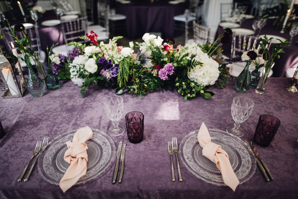 Mesa festiva que sirve con vajilla rica y flores en la mesa con paño violeta
 - Foto, imagen