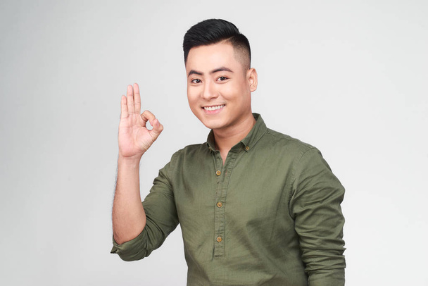 Portrait of a cheerful young asian man showing okay gesture  - Photo, Image