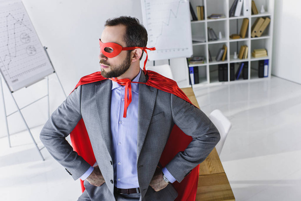высокий угол зрения супер бизнесмен в маске и плащ глядя в сторону в офисе
  - Фото, изображение