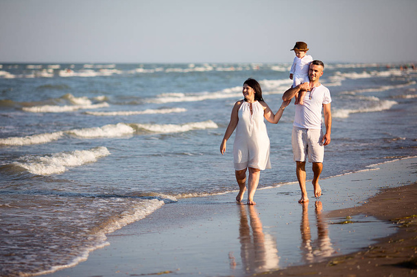 Молодая счастливая семья идет вдоль берега моря
 - Фото, изображение