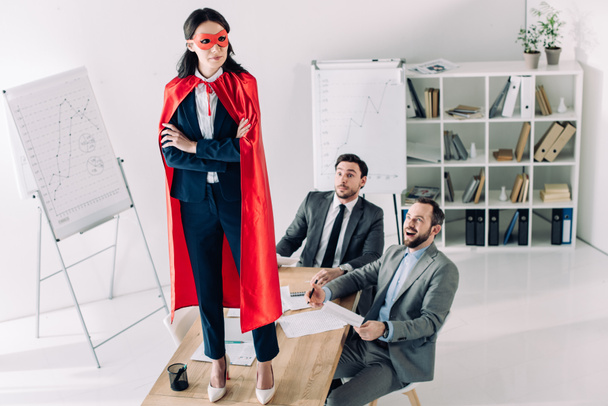 super businesswoman in mask and cape standing on table in office  - Photo, Image