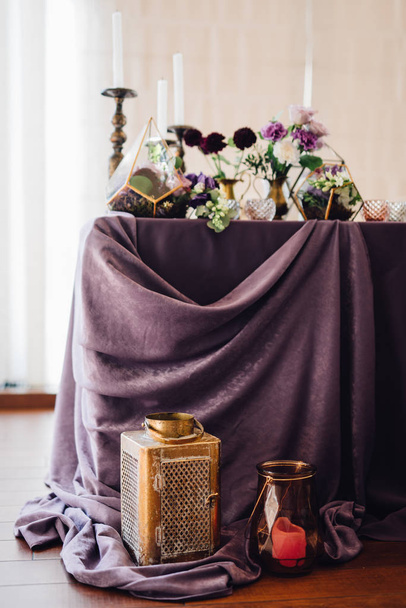 Composition of pink and violet flowers in florariums, white candles and lanterns with violet cloth  - Foto, Imagen