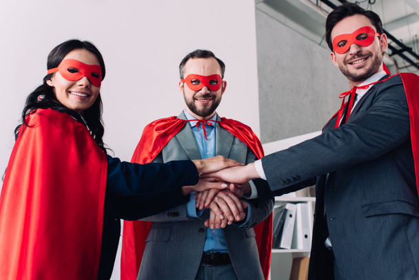super businesspeople in masks and capes putting hands together in office - Photo, Image