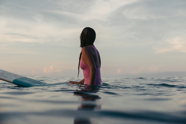 silhouette of female surfer sitting on surfboard in water at sunset - Φωτογραφία, εικόνα