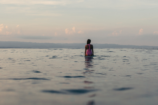 vista trasera de la silueta del surfista femenino sentado en la tabla de surf en el agua
  - Foto, Imagen
