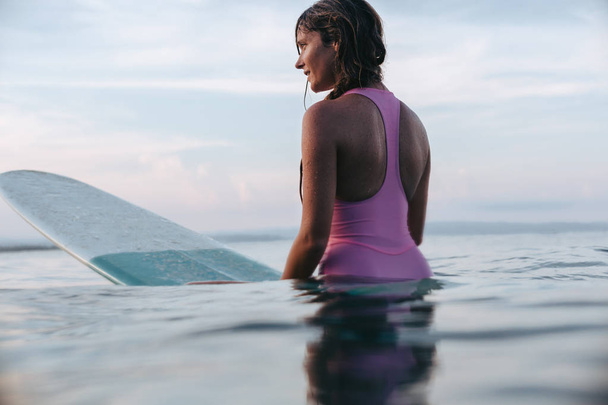 attractive woman sitting on surfboard in ocean at sunset - Foto, Imagem