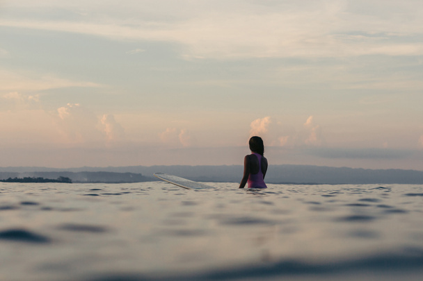 sylwetka surfer siedzi na deski surfingowej w morze o zachodzie słońca - Zdjęcie, obraz