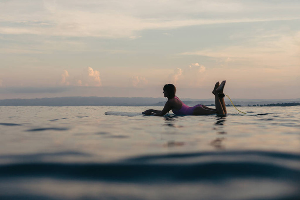 silhouette of girl lying on surfboard in water in ocean at sunset - Valokuva, kuva