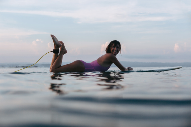 surfista sorridente sdraiato sulla tavola da surf in acqua in mare al tramonto
 - Foto, immagini