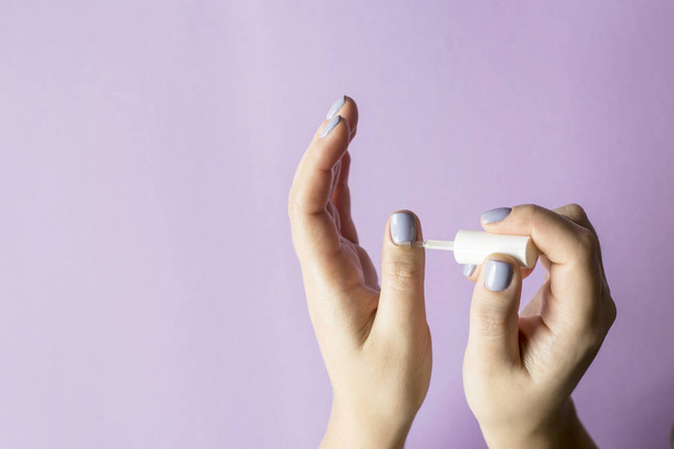 Öl für Nagelhaut. Eine Frau gießt Öl mit einer kleinen Bürste auf ihre Finger. auf leuchtend violettem Hintergrund - Foto, Bild