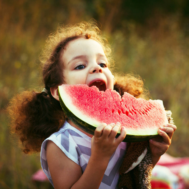 Funny portrait of an incredibly beautiful curly haired little girl eating watermelon, healthy fruit snack, adorable toddler child. Square photo - Photo, Image