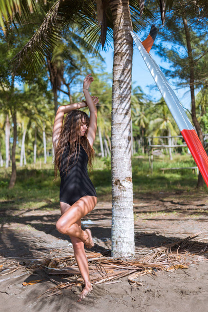 Atrakcyjna dziewczyna z długimi włosami w czarny strój kąpielowy pozowanie z deski surfingowej w pobliżu palm tree - Zdjęcie, obraz