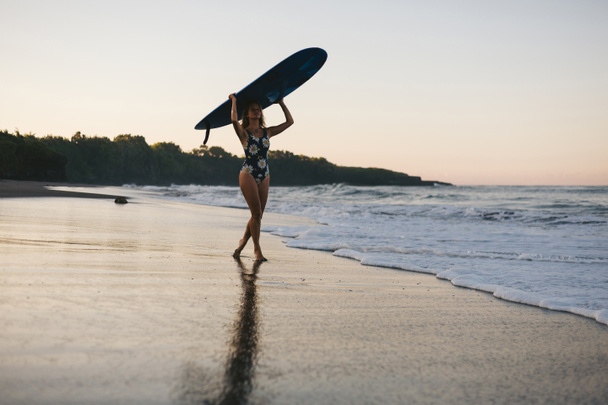 sportswoman in swimming suit with blue surfing board walking on beach - Foto, Imagem