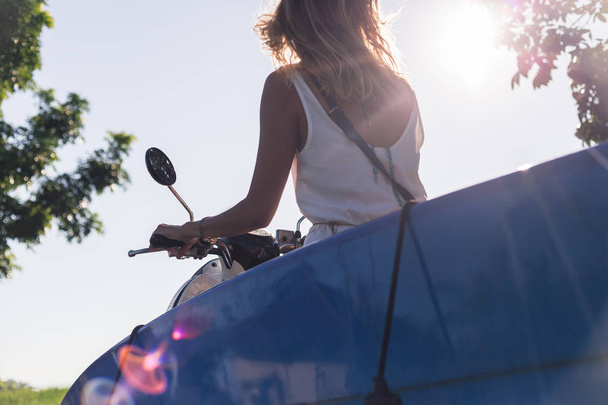 vista parcial de la mujer a caballo scooter con tabla de surf contra el cielo azul
 - Foto, imagen