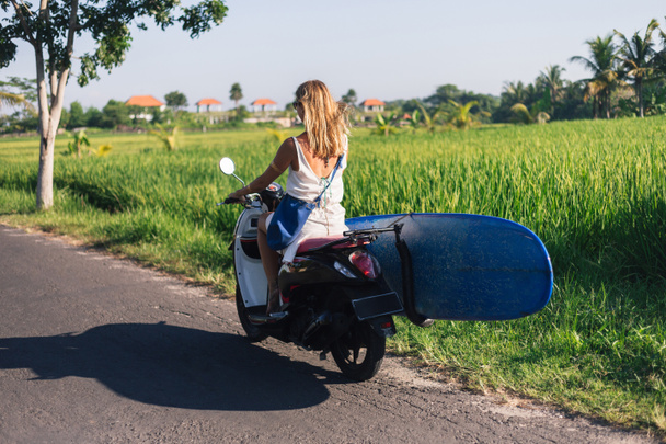 rear view of woman riding scooter with surfing board - Photo, Image