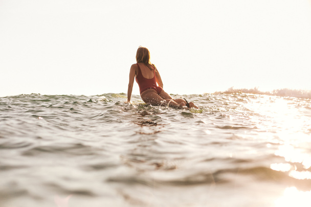back view of woman in swimming suit surfing in ocean - Zdjęcie, obraz