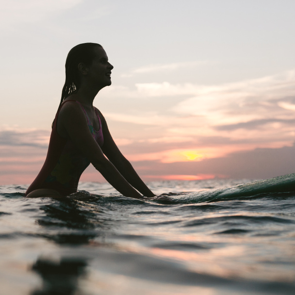 side view of silhouette of woman resting on surfing board in ocean on sunset - Photo, Image