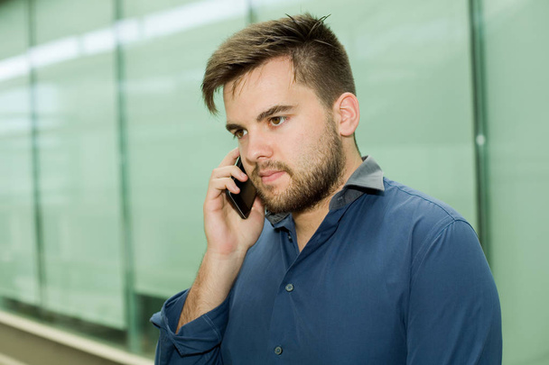 jonge casual man aan de telefoon in een kantoorgebouw - Foto, afbeelding