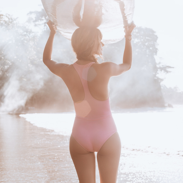 back view of sportswoman carrying surfing board on head while walking on coastline - Фото, изображение