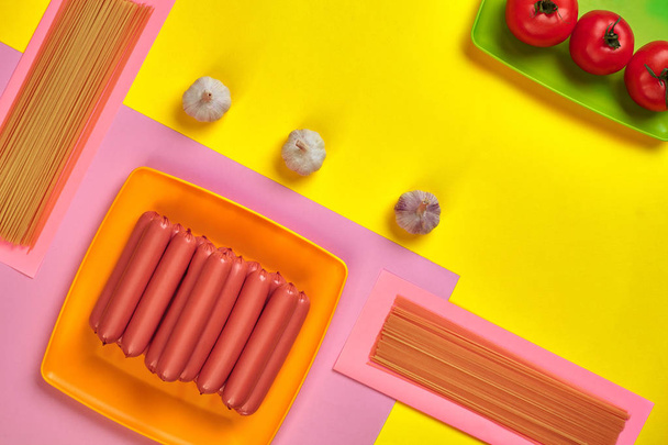 Enchidos com tomate, espaguete e alho em um fundo mínimo amarelo e rosa. Deitado. Vista superior
. - Foto, Imagem