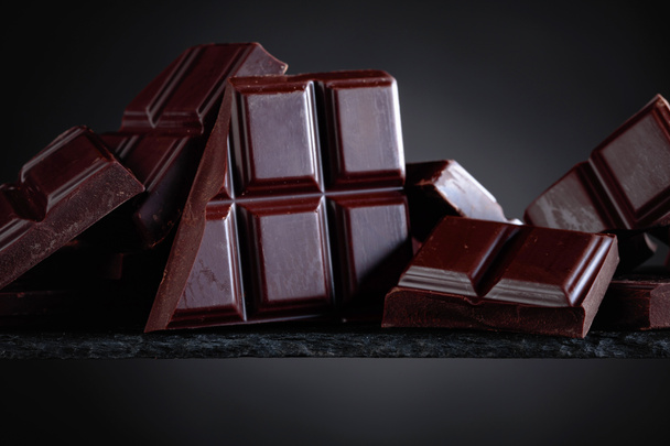 Broken chocolate pieces on a black background. - Photo, Image