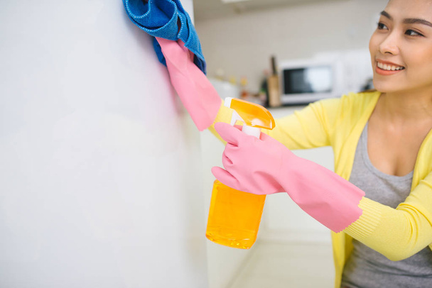 Jovem mulher asiática limpando a cozinha segurando detergente spray e pano
 - Foto, Imagem