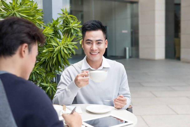 Kaksi nuorta liikemiestä rennossa vaatteissa hymyilemässä, puhumassa kahvilassa
. - Valokuva, kuva