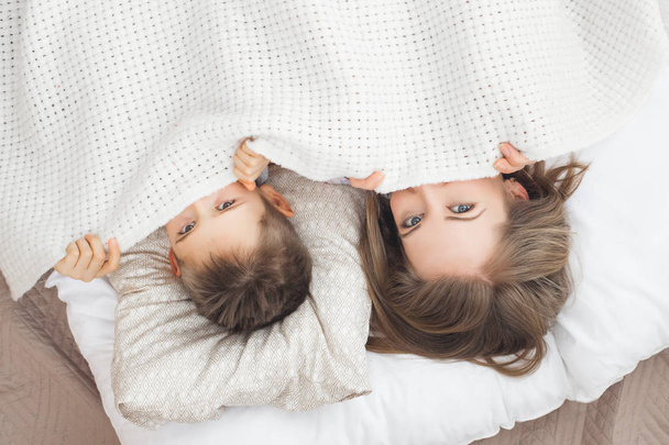 сонная мать лежит в постели с сыном под белым одеялом
 - Фото, изображение