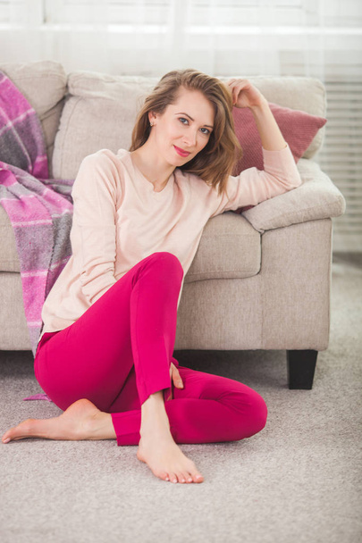 Молодая женщина в розовых джинсах сидит возле дивана
 - Фото, изображение