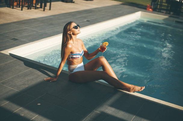 Mujer joven bebiendo cóctel en la piscina en el caluroso día de verano
 - Foto, imagen
