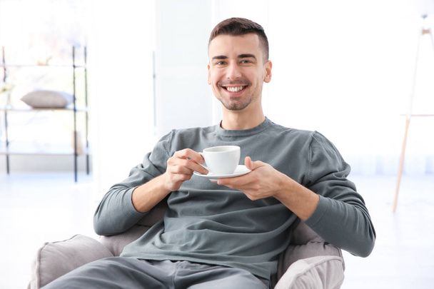 Young man sitting in armchair and holding cup of coffee - Foto, Imagem