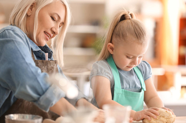 Little girl and her grandmother preparing dough together on kitchen - Zdjęcie, obraz