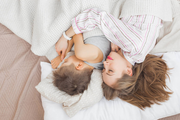 Mother sleeping with son in bed under white blanket  - Foto, Bild