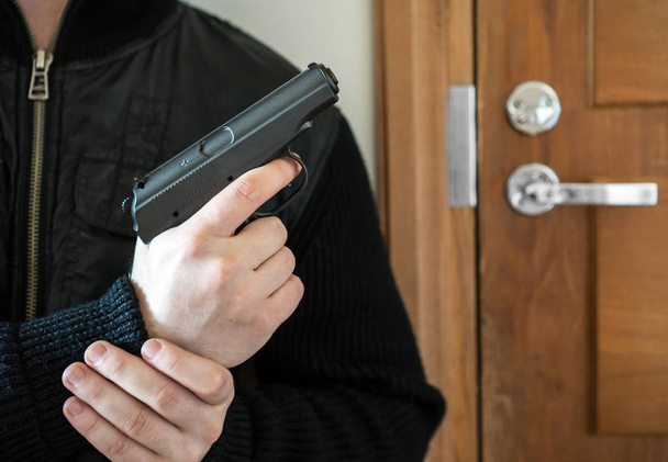 Вооруженный человек с пистолетом ждет свою жертву возле двери
. - Фото, изображение
