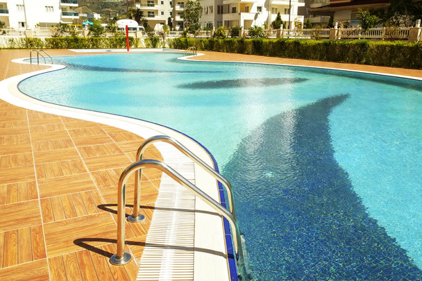 Área de piscina de novo complexo residencial de luxo com azulejos, alças de escadas cromadas e drenos. Dia lindo ensolarado
. - Foto, Imagem