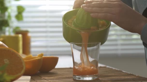 Woman preparing an healthy fresh orange juice for morning breakfast in the kitchen, she is pouring the juice in a glass, healthy food concept - Filmati, video