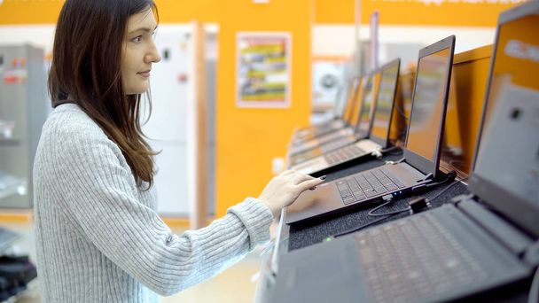 Nuori brunette nainen valitsee kannettavan tietokoneen rautakaupasta
 - Valokuva, kuva