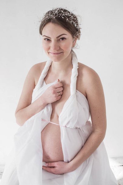 photo pregnant girl in white drapery white background portrait - Photo, Image