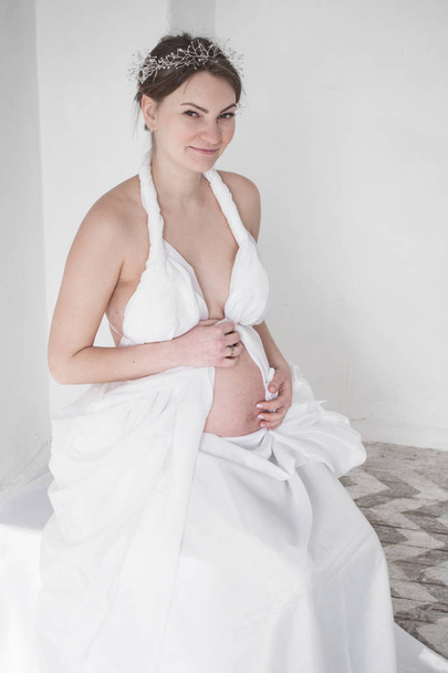 photo pregnant girl in white drapery white background - Photo, Image