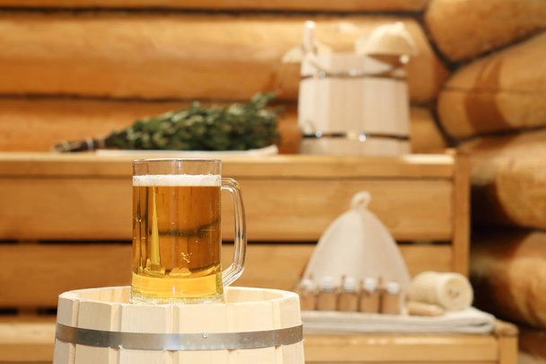 A mug of  light beer on a barrel in the sauna on the background of bath accessories. - Photo, Image